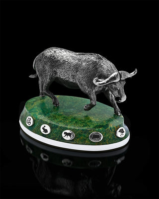 Bronze bull sculpture on a green marble base with symbols, against a black background