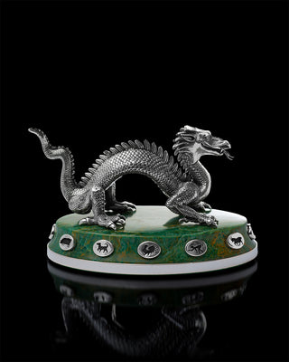 Silver dragon figurine on a green base with circular designs against a black background