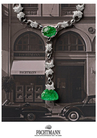 Luxury necklace with green emerald gemstones in front of a Fochtmann store.