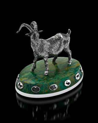 Decorative figurine of a goat on a green stone base with symbols, against a black background.