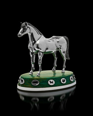 Metallic horse figurine on a green base with emblem details against a black background