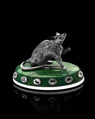 Silver rat figurine on a green pedestal with symbols against a black background