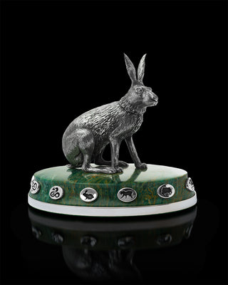 Bronze hare sculpture on a green marble base with decorative elements against a black background