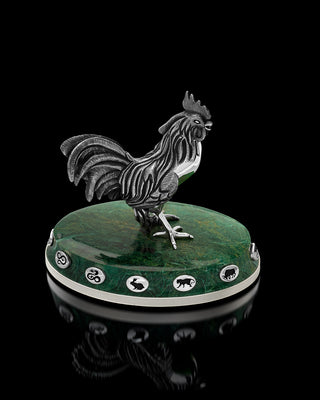 Decorative rooster figurine on a green base with symbols, against a black background