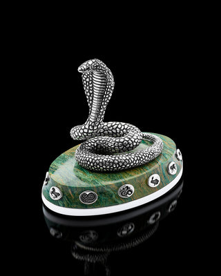 Silver snake sculpture on a green base with decorative elements against a black background